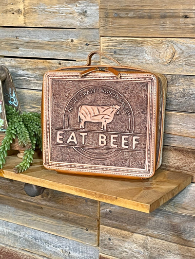 Leather jewelry case with 'Eat Beef' text on a wooden shelf against a rustic wooden wall.