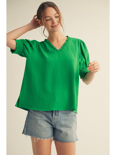 Woman wearing a green blouse and denim shorts on a beige background