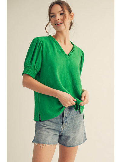 Woman wearing a green blouse and denim shorts on a plain background