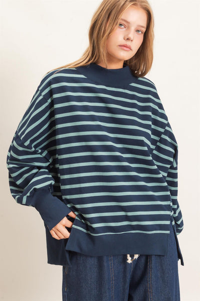 woman wearing a navy/sage striped sweatshirt and jeans with a light background