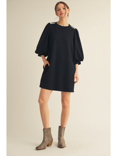 Woman wearing a black dress with balloon sleeves on a beige background