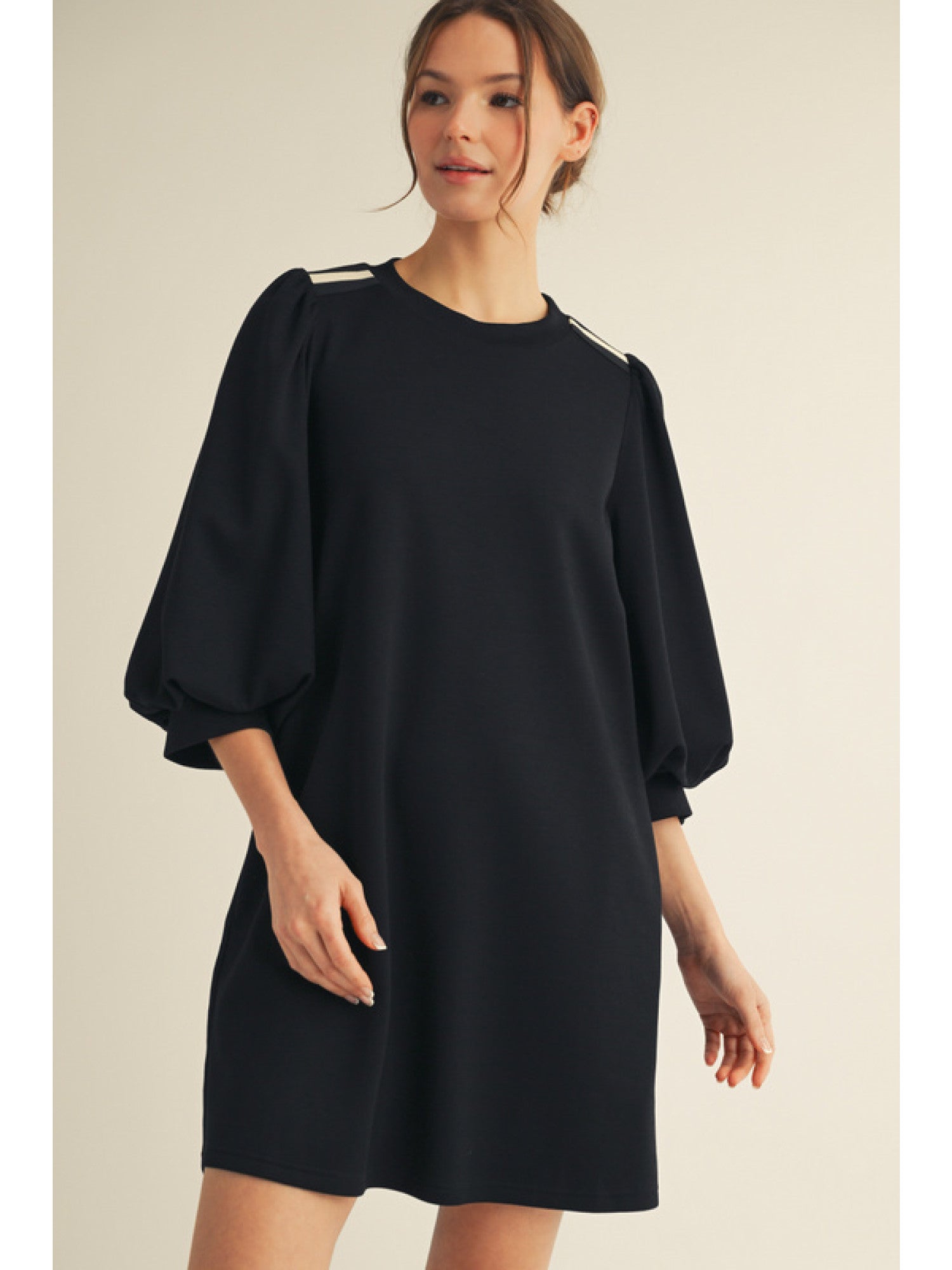 Woman wearing a black dress with puff sleeves on a beige background