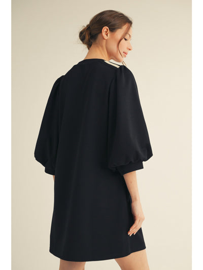 Woman wearing a black dress with balloon sleeves on a beige background