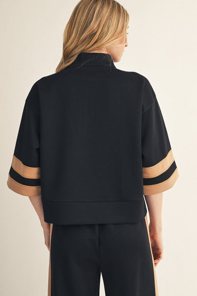 Back of woman wearing a black and beige outfit with a plain background