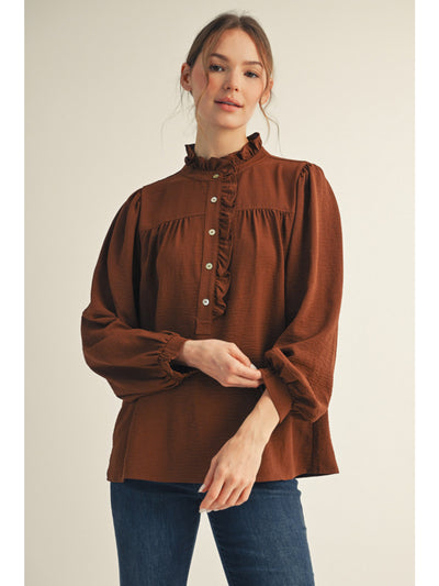 Woman wearing a brown blouse with long sleeves and a high collar on a beige background