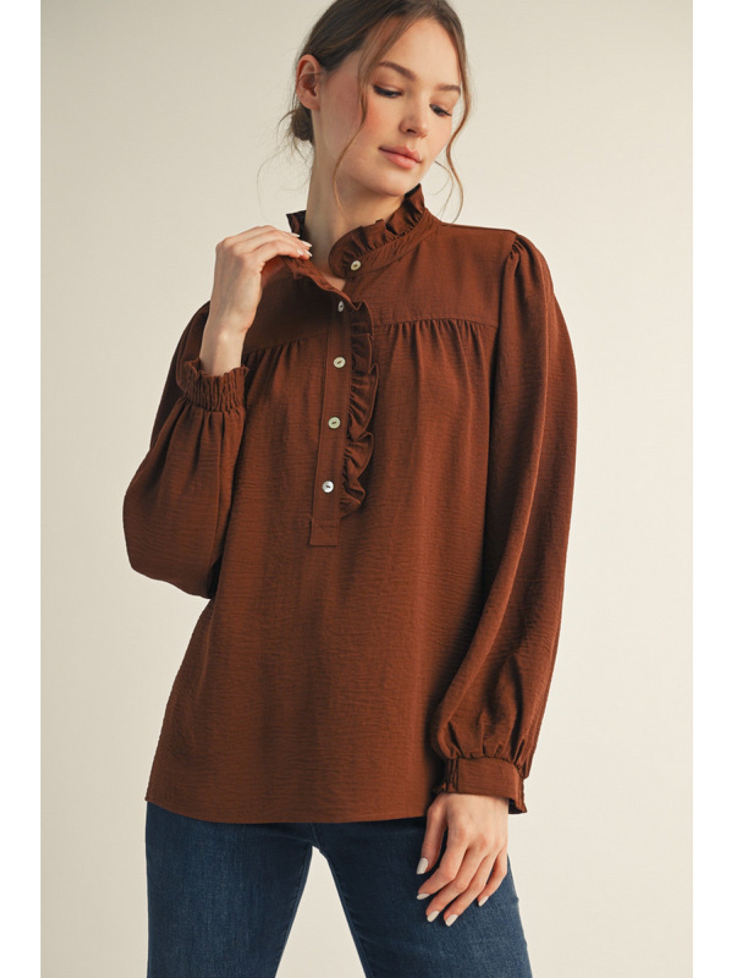 Woman wearing a brown blouse with ruffled collar against a beige background
