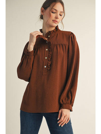 Woman wearing a brown blouse with ruffled collar against a beige background