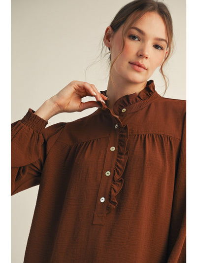 Woman wearing a brown blouse with ruffled details on a plain background