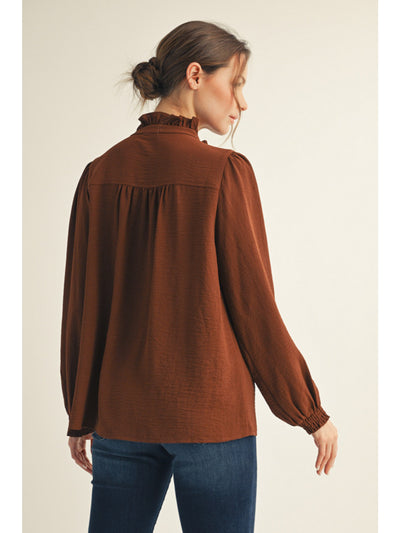 Woman wearing a brown blouse with long sleeves on a beige background