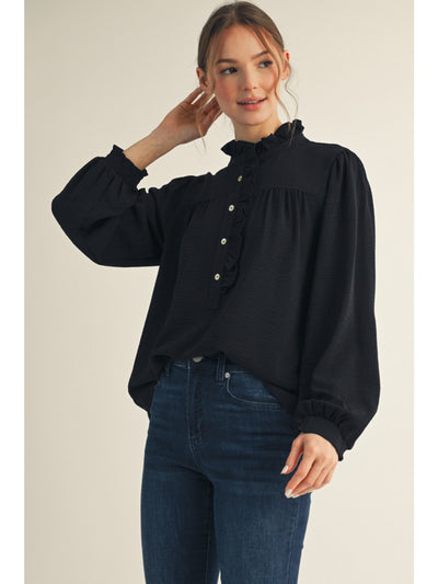 Woman wearing a black blouse with a ruffled collar and blue jeans on a beige background