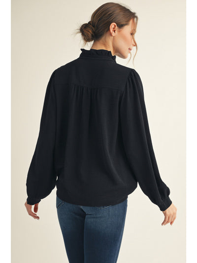 Woman wearing a black blouse with long sleeves and a high collar on a beige background