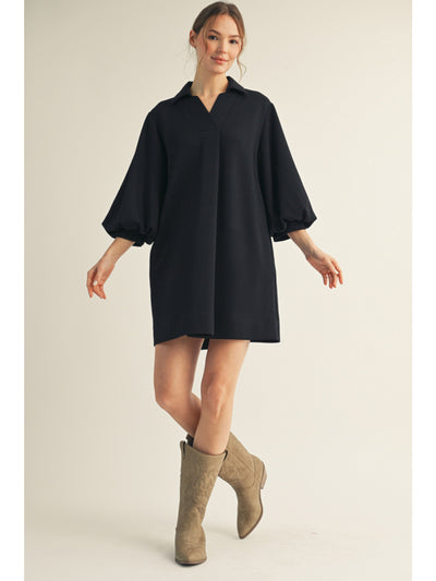 Woman wearing a black dress with balloon sleeves and beige boots on a light background