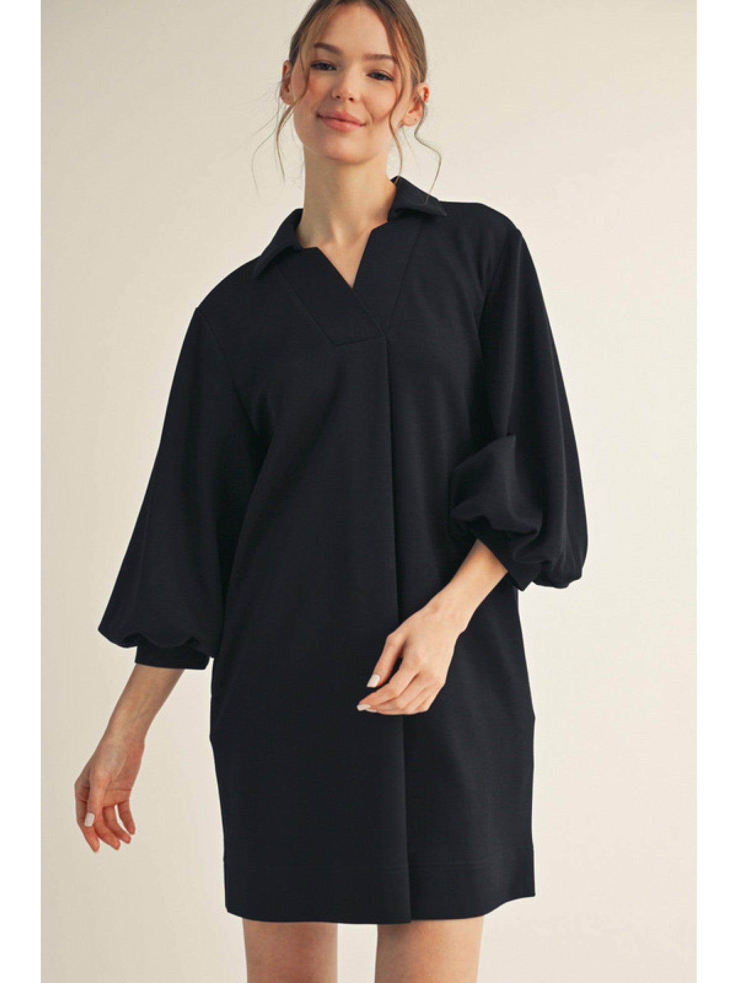 Woman wearing a black dress with balloon sleeves on a beige background