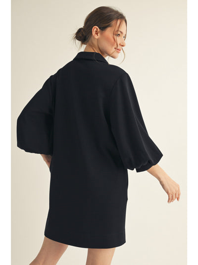 Woman wearing a black dress with wide sleeves on a beige background