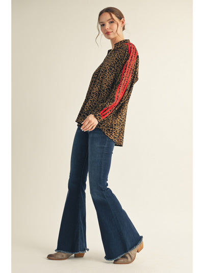 Woman wearing a leopard print top with red accents and blue jeans on a beige background