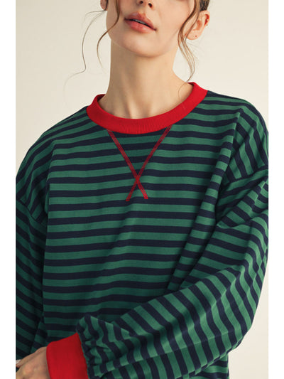 Person wearing a green and navy striped sweater with red trim on a plain background