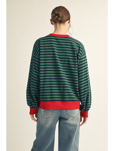 Person wearing a green and red striped sweater with blue jeans on a beige background