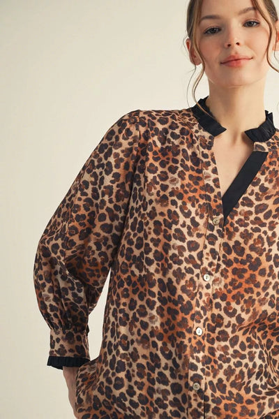Woman wearing a leopard print blouse with black trim on a beige background