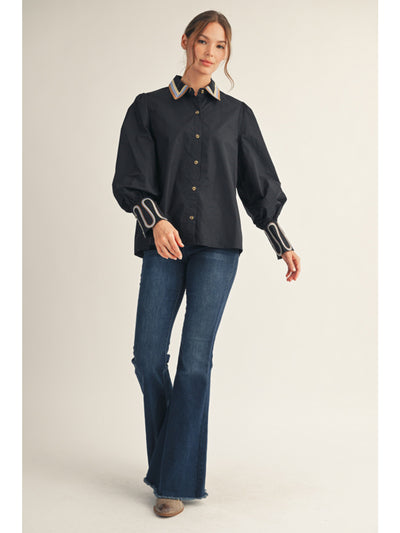 Woman wearing a black shirt with white trim and blue jeans on a beige background