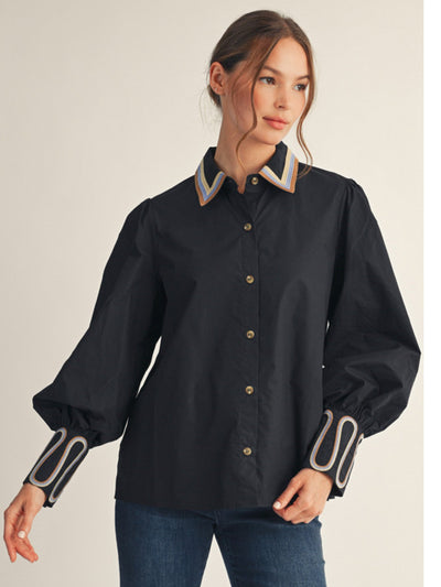 Woman wearing a black shirt with decorative cuffs and collar against a beige background