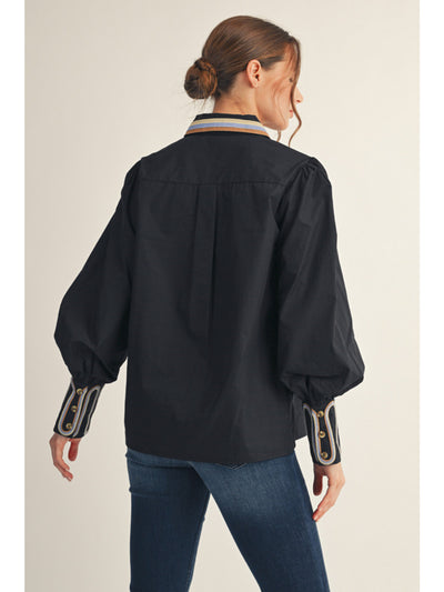 Woman wearing a black blouse with decorative cuffs on a beige background