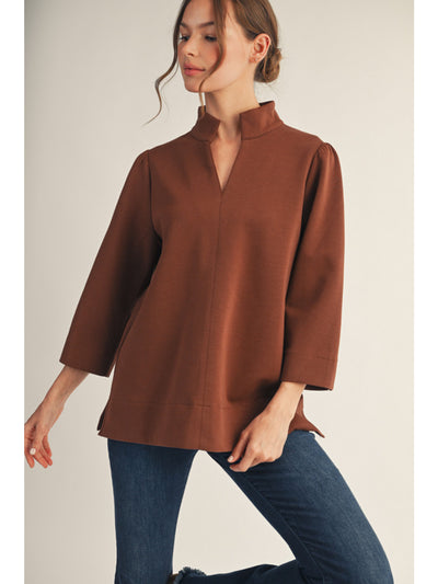 Woman wearing a brown blouse and blue jeans against a plain background