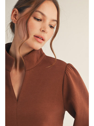 Woman wearing a brown long-sleeve top against a neutral background