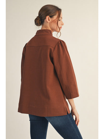 Woman wearing a brown jacket and blue jeans on a plain background