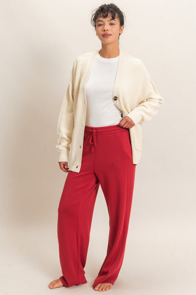 model wearing a white shirt, ivory cardigan & red pants with a light background