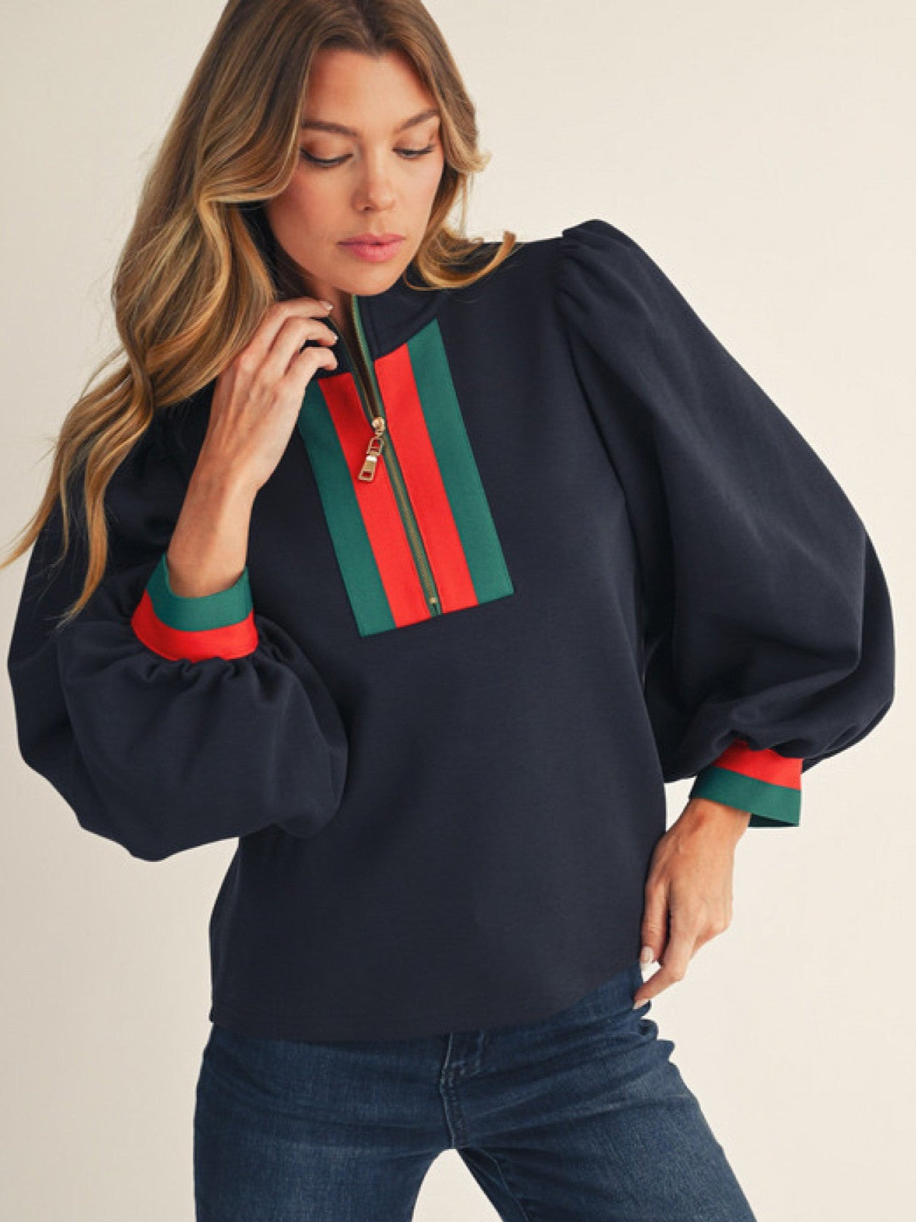Woman wearing a navy sweater with red and green zipper details on a beige background