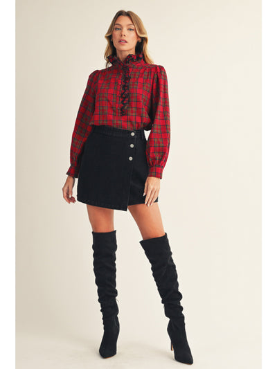 Woman wearing a red plaid shirt, black skirt, and black knee-high boots on a beige background