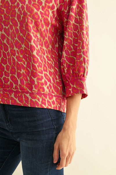 A close-up of a person wearing a pink  leopard-print long-sleeve top with dark blue jeans, shown against a plain light background.