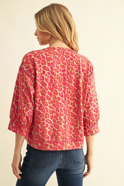 A woman shown from the back wearing a pink and beige leopard-print cropped jacket with three-quarter sleeves, paired with dark blue jeans, against a solid cream background.