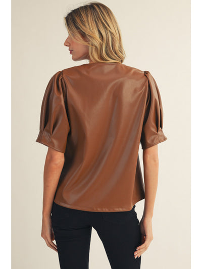 Woman wearing a brown leather-like top against a beige background