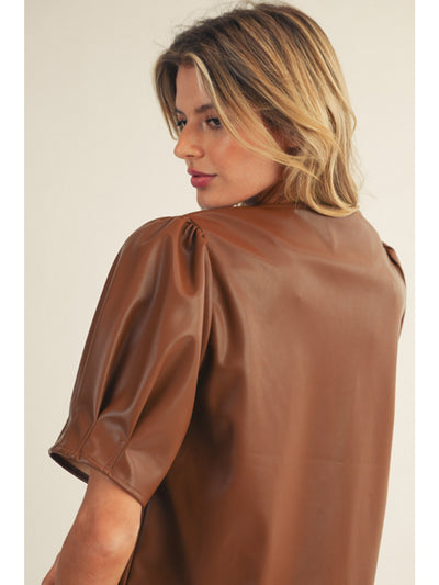 Woman wearing a brown leather blouse against a plain background