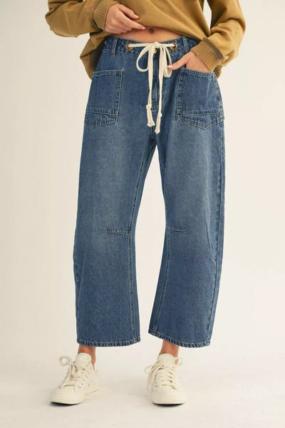 Person wearing blue jeans with a drawstring and white sneakers on a beige background