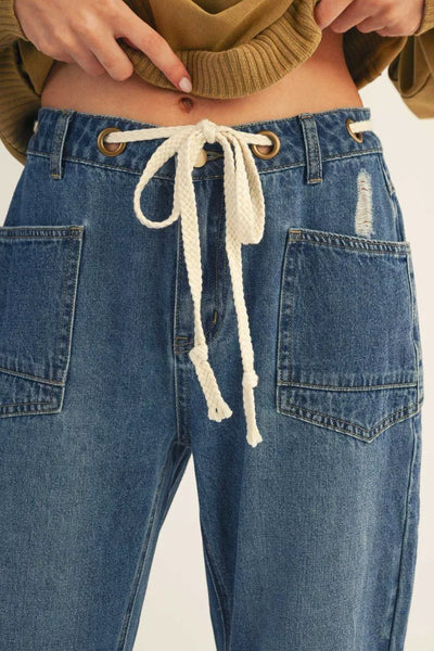 Close-up of blue jeans with a drawstring and a brown sweater.