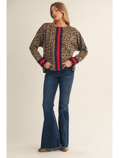 Woman wearing a leopard print sweater with red and blue stripes and blue jeans on a beige background