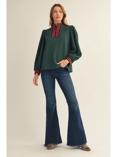 Woman wearing a green sweater with red accents and blue jeans on a beige background