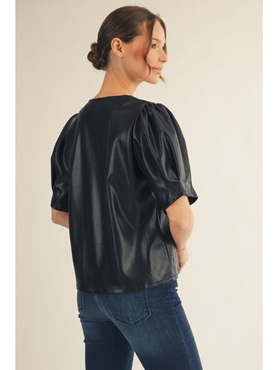 Woman wearing a black leather-like top and blue jeans on a plain background