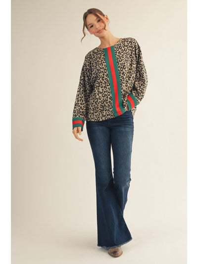 Woman wearing a leopard print sweater with red and green stripes and blue jeans on a beige background