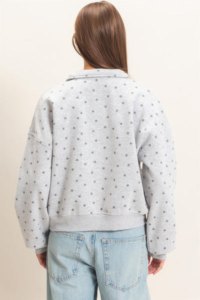 back of model wearing gray half zip sweatshirt with stars and jeans before a light background
