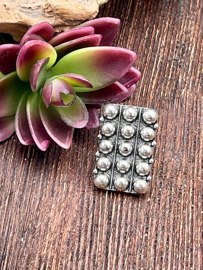 Silver ring with raised circular patterns on a wooden surface with succulent plant.