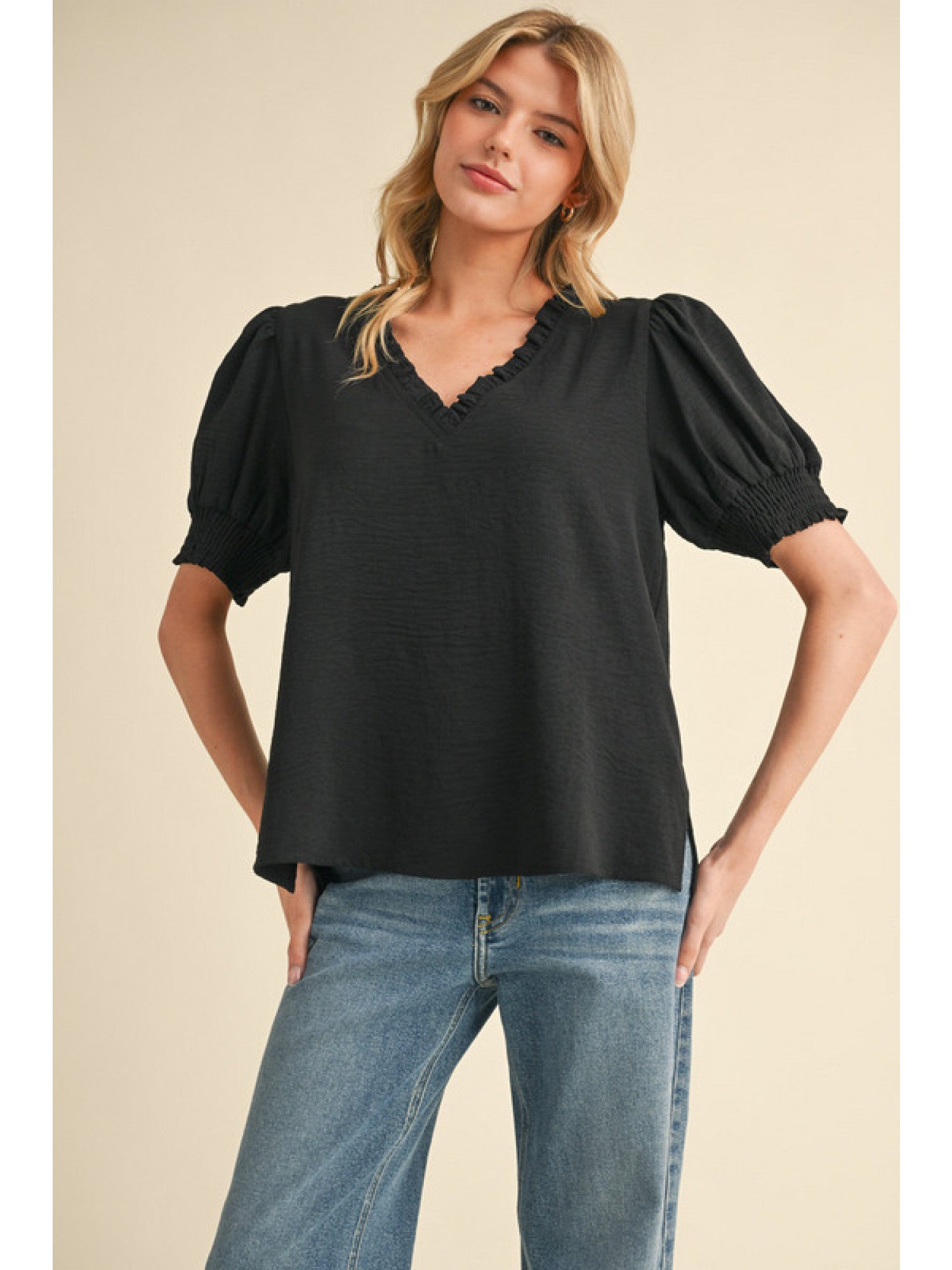 Woman wearing a black blouse with puff sleeves and blue jeans on a beige background