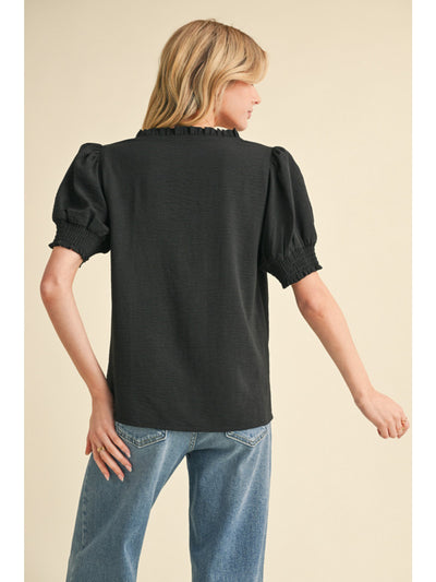 Woman wearing a black blouse with puff sleeves and blue jeans on a beige background