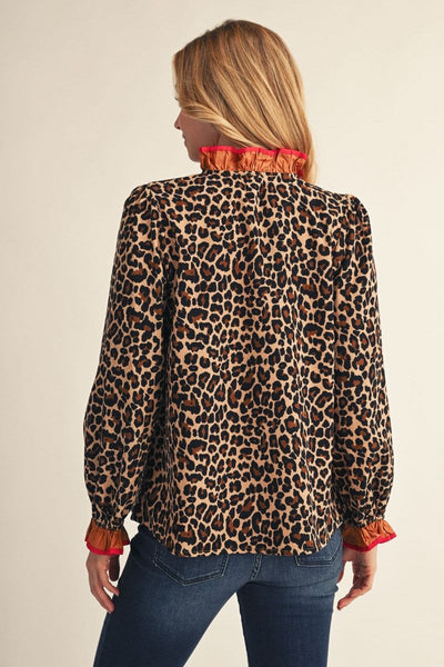 A woman shown from the back wearing a leopard print blouse with a bright red ruffled collar and cuffs, paired with blue jeans, against a plain beige background.