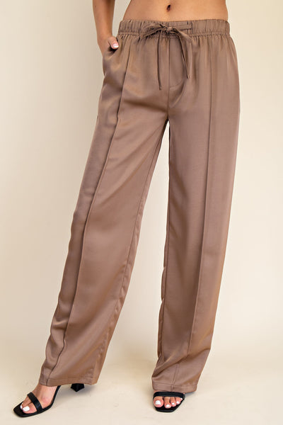 Brown satin pants worn by a person on a beige background