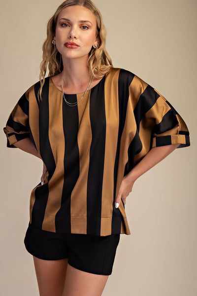 Woman wearing a black and gold striped top with black shorts on a beige background