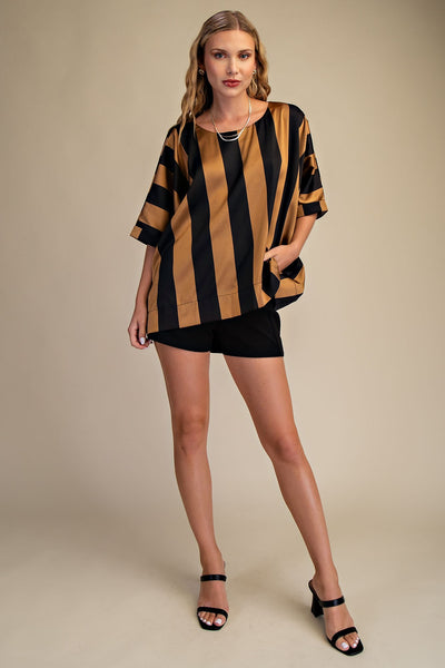 Woman wearing a black and gold striped top with black shorts on a beige background