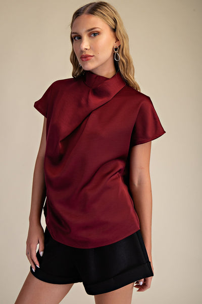 Woman wearing a burgundy top with a draped design on a beige background
